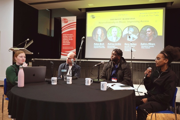 Four people sitting at a table with microphones, discussing topics during a workshop / panel.