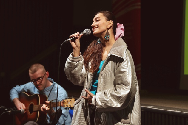 A woman passionately singing into a microphone as a man skillfully plays the guitar beside her.
